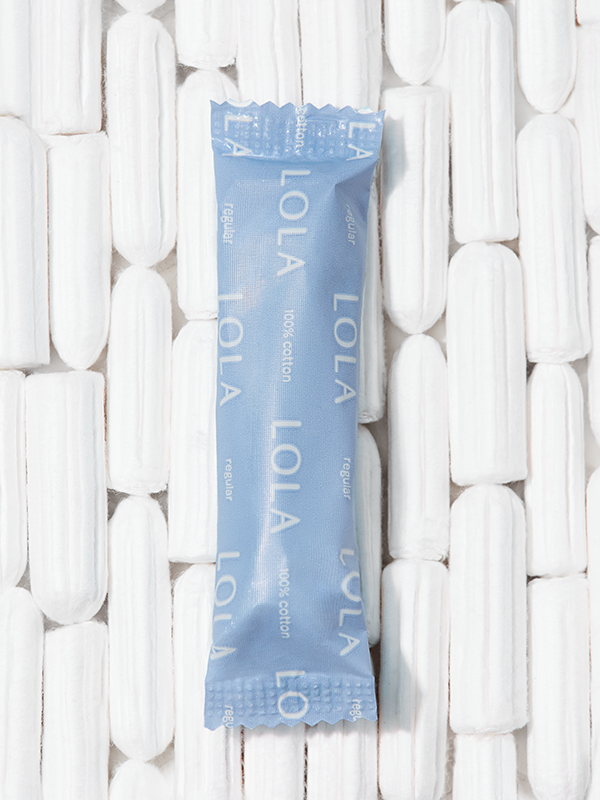 Compact plastic applicator tampons | 1 regular tampon in packaging against a background of unwrapped tampons